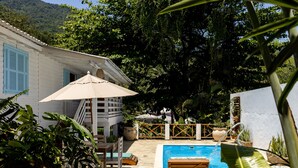 Een zwembadgedeelte met een houten terras, ligbedden en een pergola met een parasol.