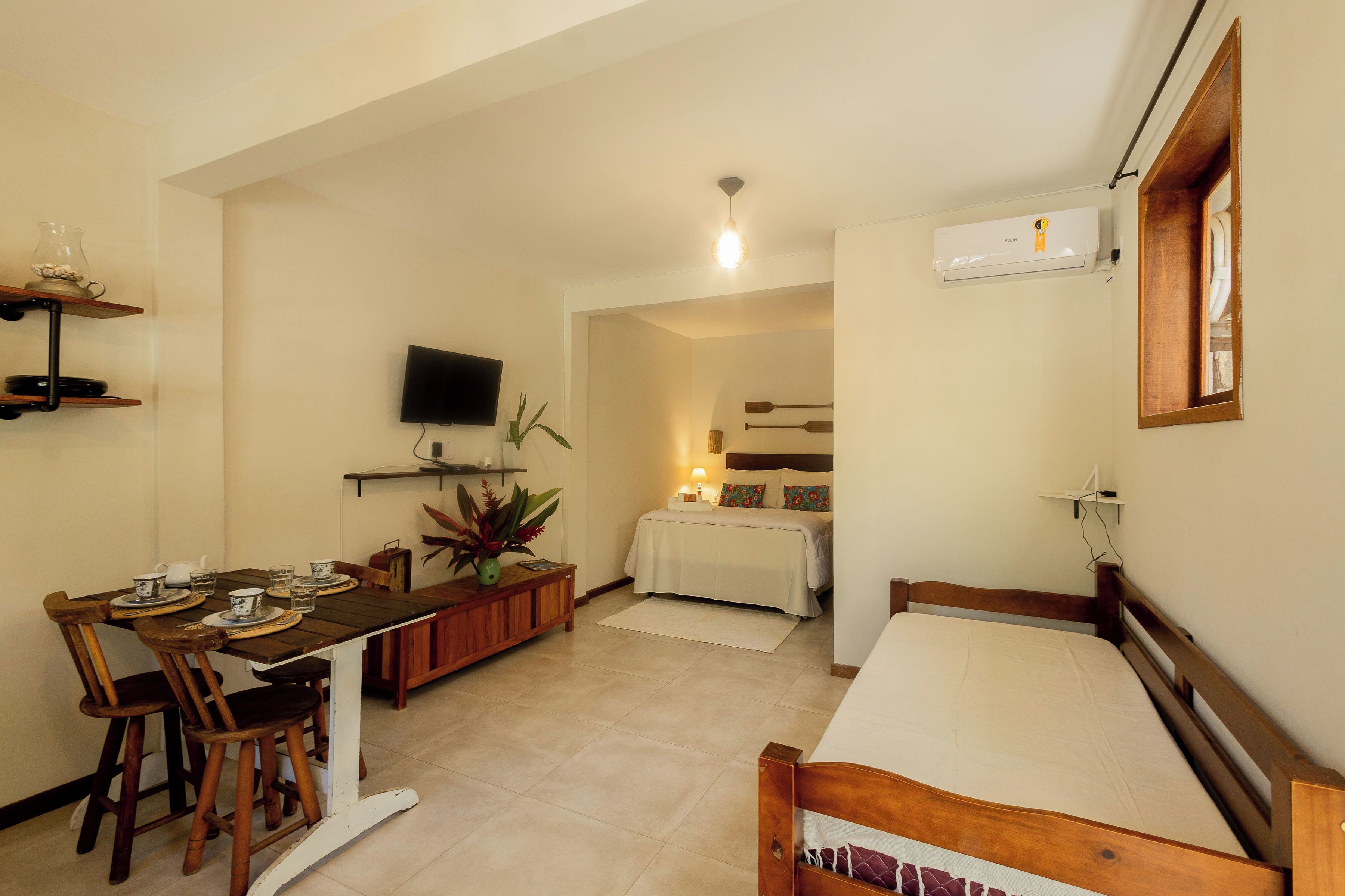 A compact room with a bed, a dining table with chairs, a TV, and a small kitchenette.