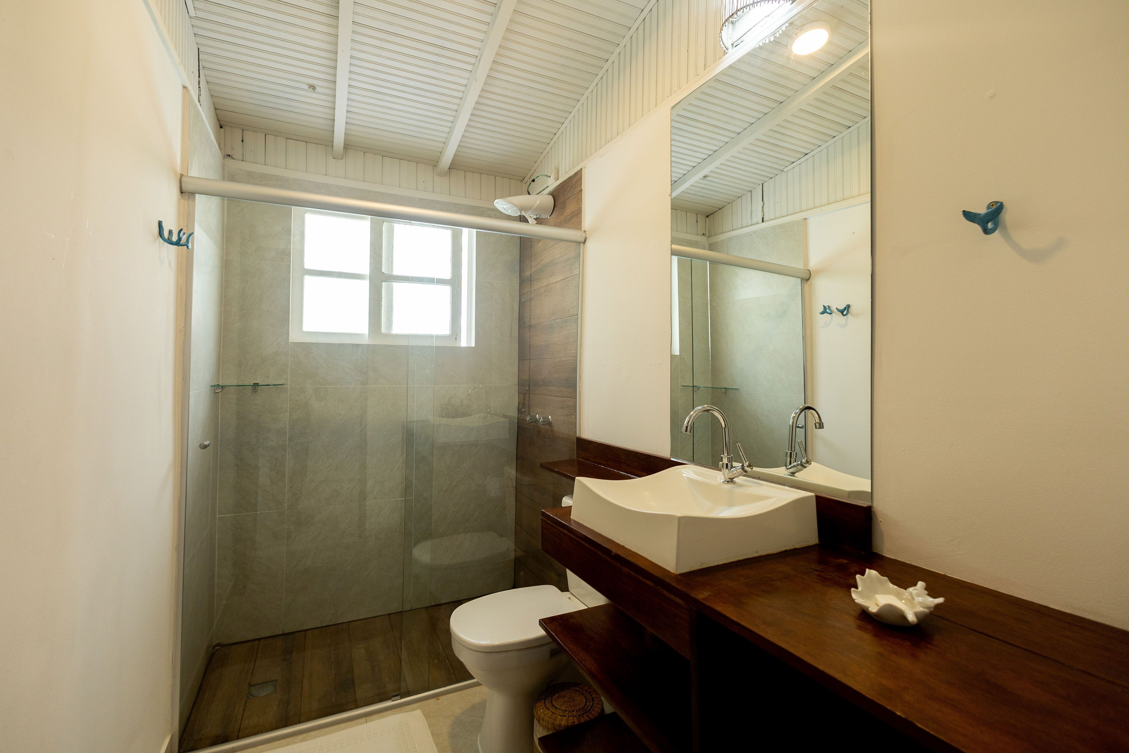 A modern bathroom with a glass shower enclosure, a white toilet, a wooden vanity with a sink, and a large mirror.