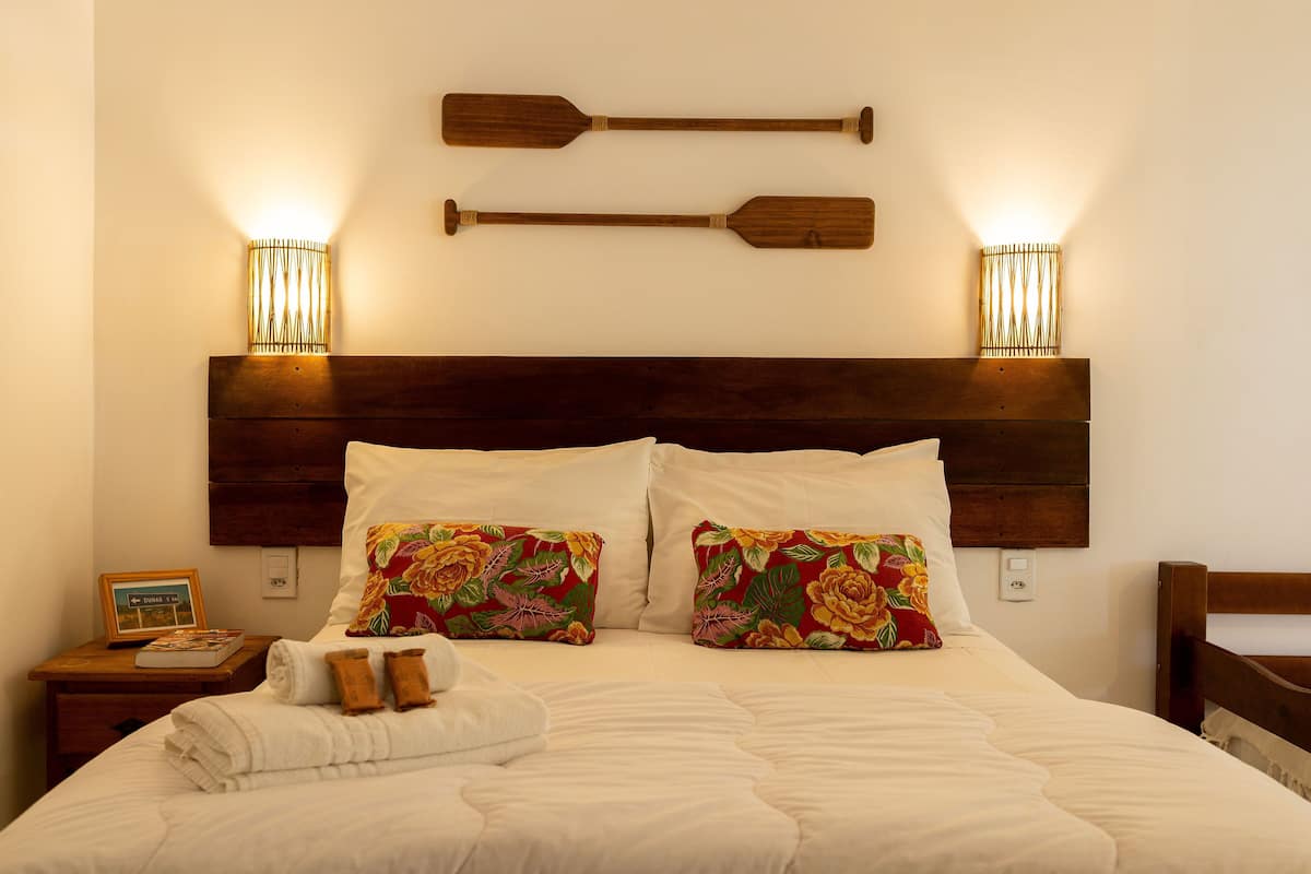 A neatly made bed with white bedding, two decorative pillows with floral patterns, and two wooden paddles mounted on the wall above.