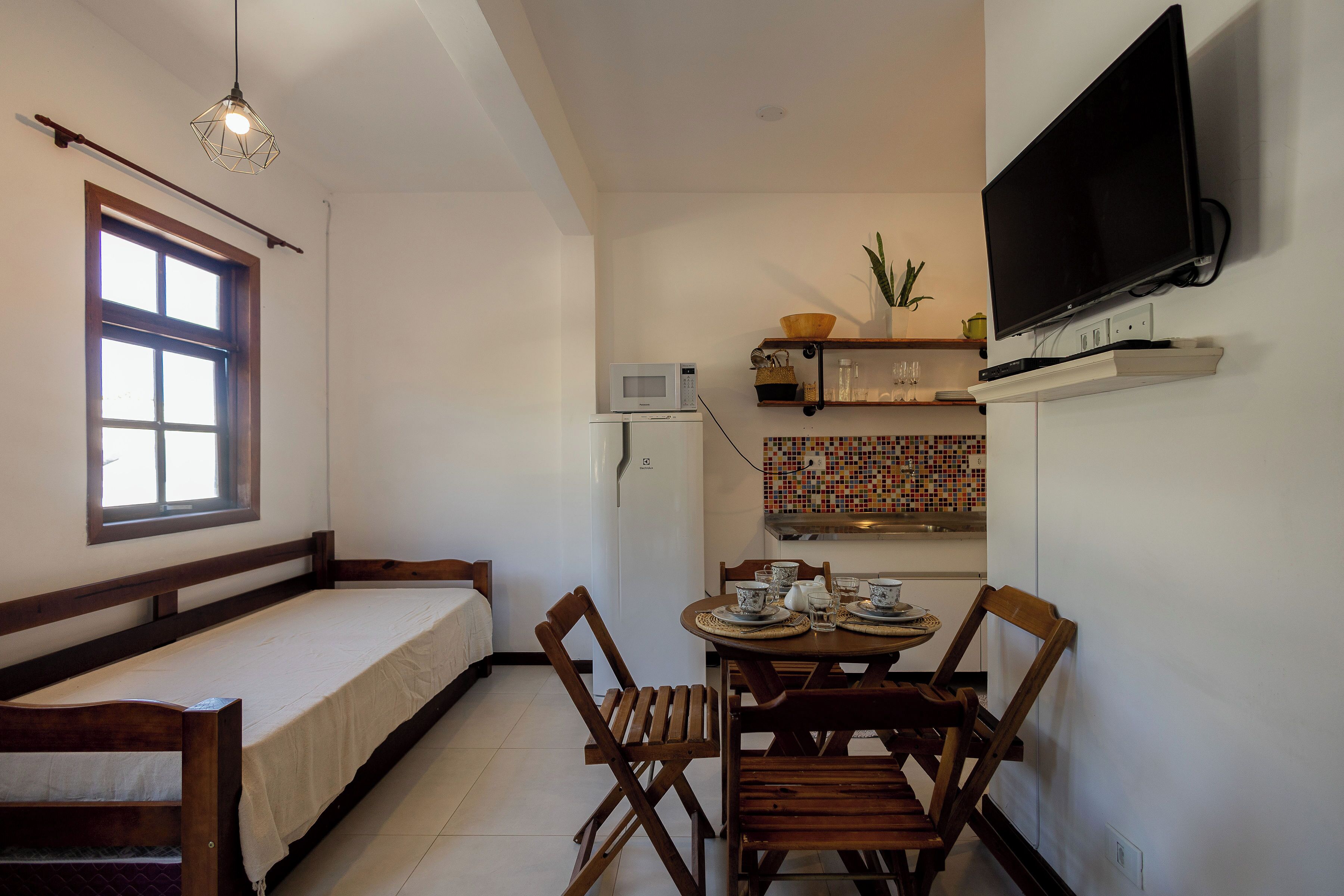 A compact room with a bed, a dining table with chairs, a TV mounted on the wall, and a microwave on the counter.