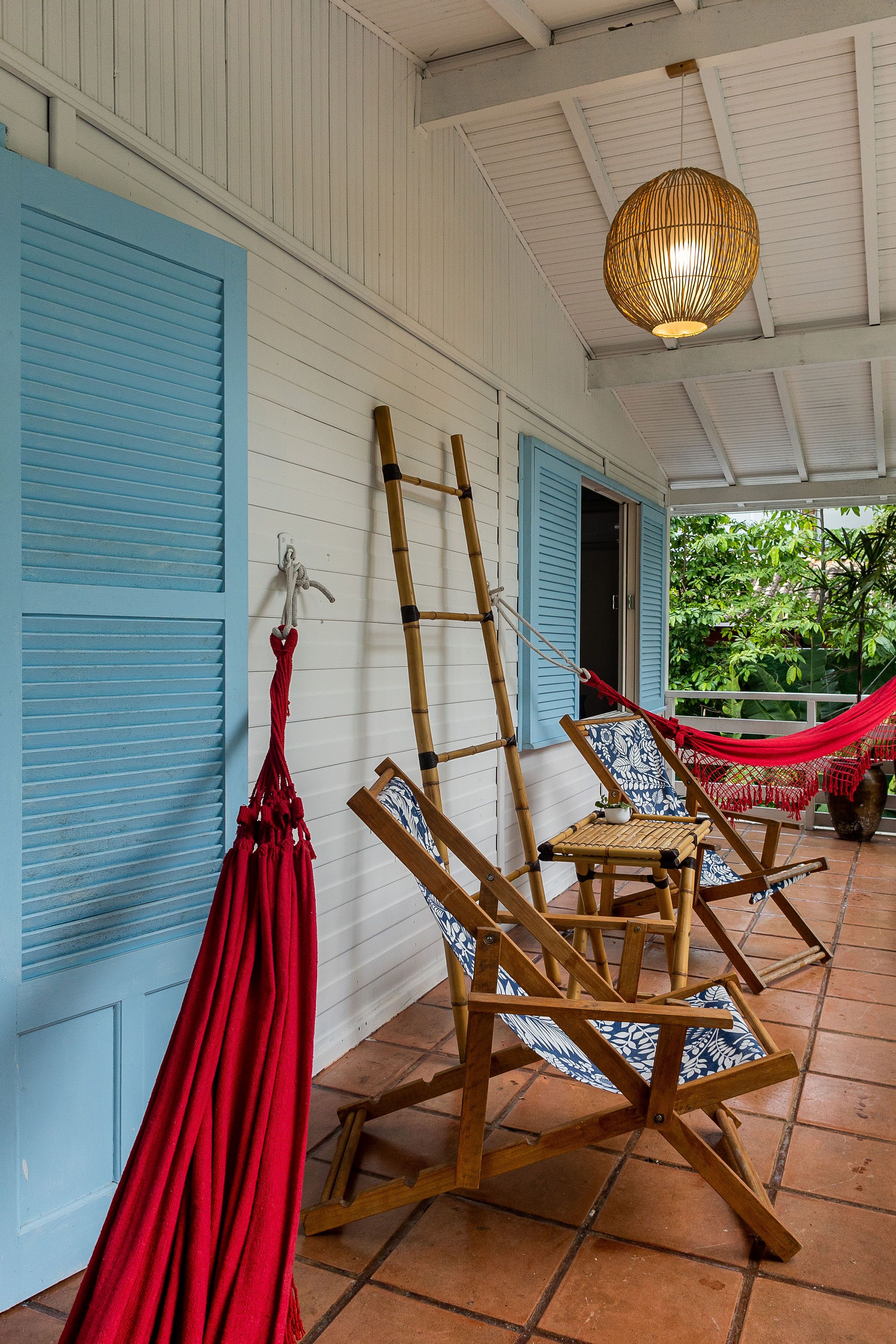 A covered porch with blue shutters, a hammock, and two wooden chairs with patterned cushions.