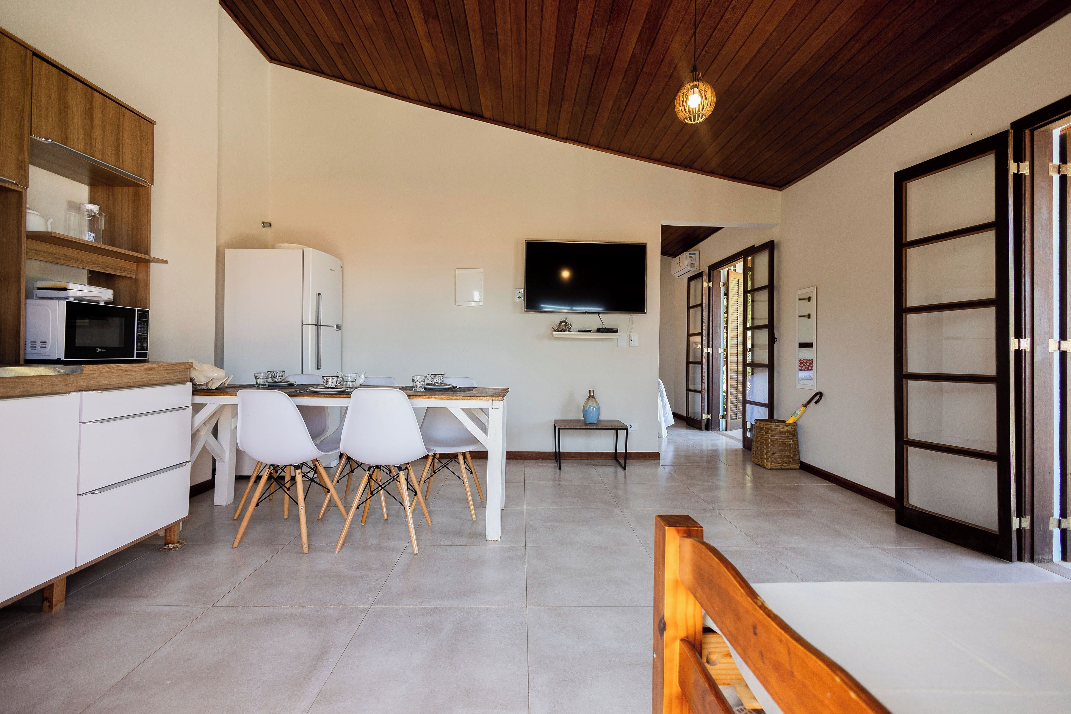Una cocina moderna con electrodomésticos blancos, un comedor con mesa y sillas de madera, y un televisor montado en la pared.