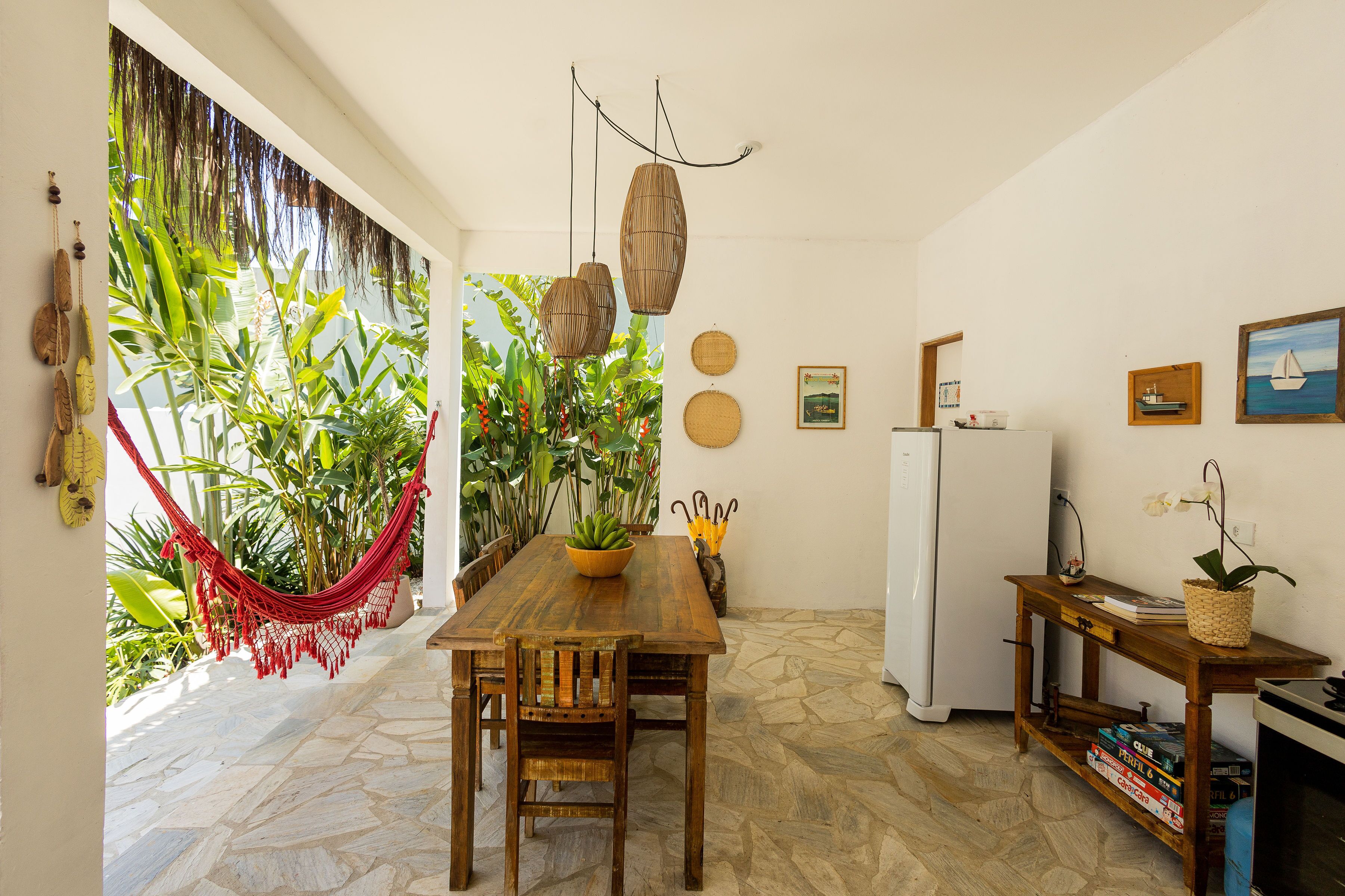 A compact kitchen with a wooden table, chairs, a refrigerator, and a small shelf with books and a plant.