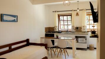 A bedroom with a wooden bed, a dining area with chairs and a table, a kitchen with a stove and microwave, and a window with curtains.