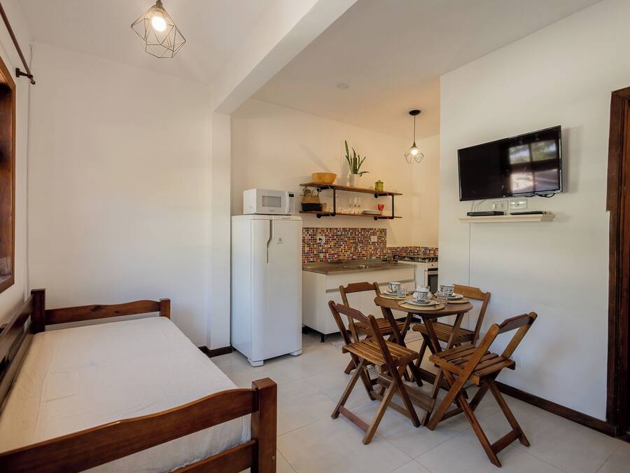 A compact kitchen with a microwave, refrigerator, and a TV mounted on the wall. There is a dining area with wooden chairs and a table.