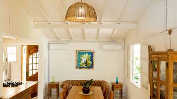 A dining area with a wooden table, chairs, a hanging light fixture, a painting on the wall, and a window with a view.