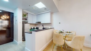 A modern kitchen with white cabinets, a black refrigerator, and a glass dining table with four chairs. - GreenFuture - Elegant Apartment With Balcony Near The Walk JBR  (Dubai)