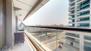 A balcony with a hanging chair, a table, and a view of a highway and buildings. - GreenFuture - Elegant Apartment With Balcony Near The Walk JBR  (Dubai)