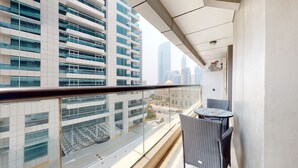 Uma varanda com vista para edifícios modernos, guarda-corpo de vidro e uma mesa pequena com cadeiras.