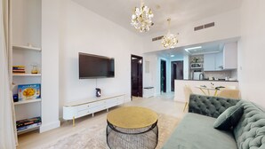 Uma sala de estar moderna com uma TV de tela plana, uma mesa de centro redonda e um sofá. Há uma área de cozinha com micro-ondas e armários.