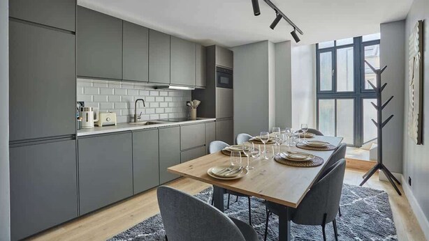 A modern kitchen with grey cabinets, a wooden dining table set for six, and a large window providing natural light. - Sublime and new apartment Le Marais / Beaubourg (Paris)
