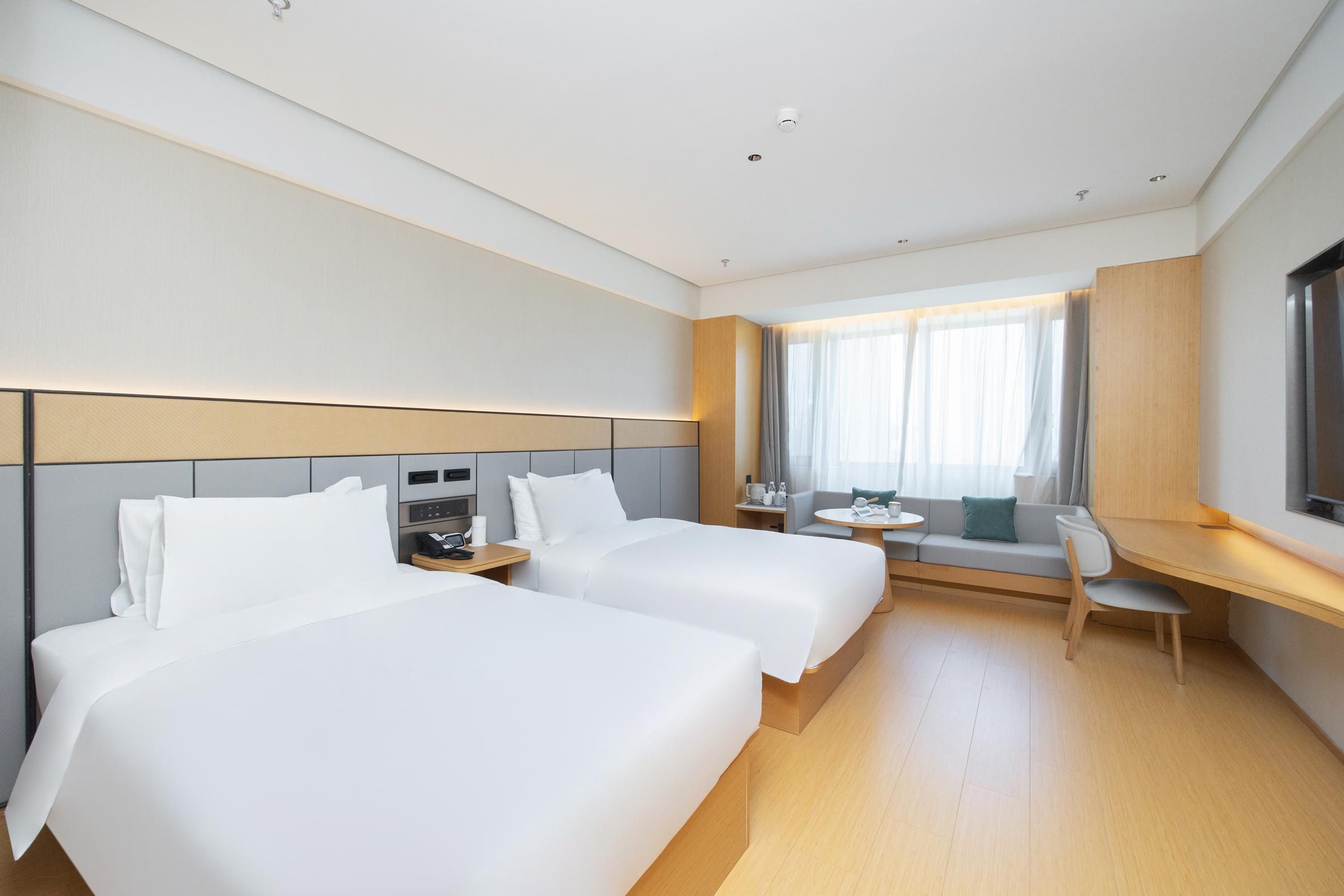 A hotel room with two beds, a desk, a chair, and a TV.