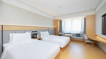 A hotel room with two beds, a desk, a chair, and a TV.