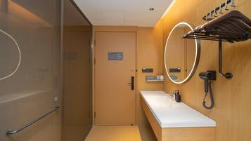 Un baño moderno con cabina de ducha de vidrio, tocador de madera con encimera blanca y toallero con una toalla colgada.