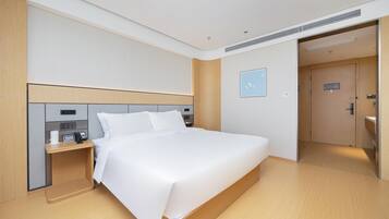 Una habitación de hotel moderna con una cama grande, una mesita de noche con teléfono y cafetera, un cabecero de madera, y una puerta que da a un baño.