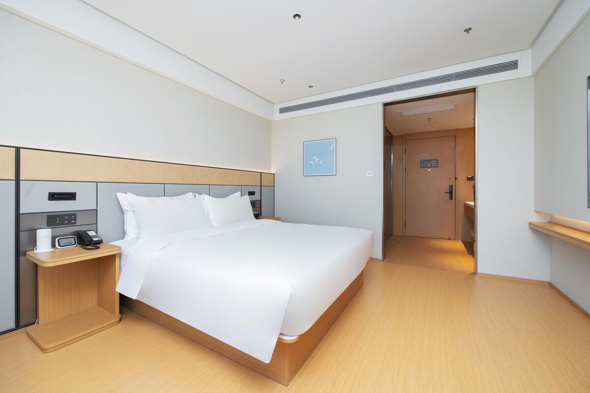 A hotel room with a bed, bedside table, and a phone. There is a door leading to a bathroom.
