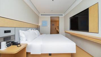 A hotel room with a bed, bedside table, TV, and a door leading to a bathroom.