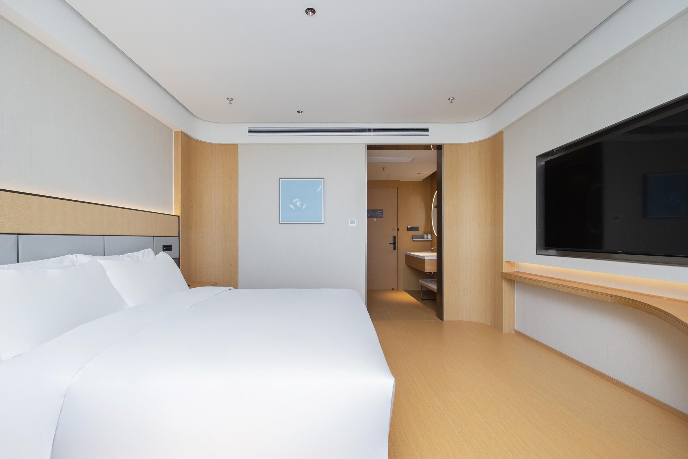 Una habitación de hotel moderna con una cama grande, un televisor y un baño visible a través de una puerta abierta.