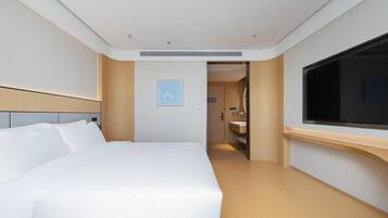Una habitación de hotel moderna con una cama grande, un televisor y un baño visible a través de una puerta abierta.