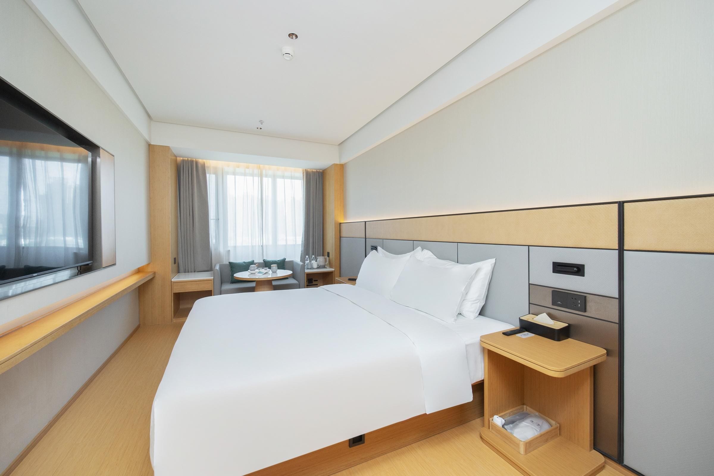 A hotel room with a large bed, bedside tables, a desk, and a window with curtains.