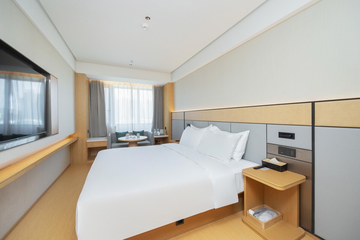 A modern hotel room with a large bed, bedside tables, a desk, and a TV.