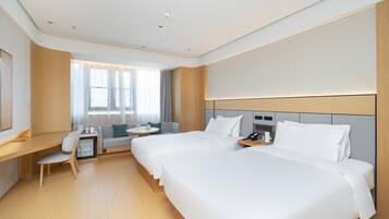 A hotel room with two beds, a desk, a chair, a small table, and a window with curtains.