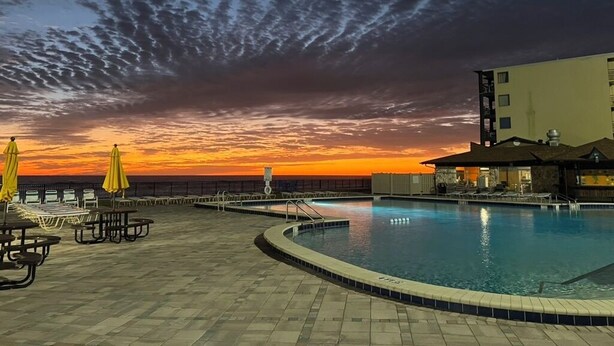 A pool area with lounge chairs and umbrellas, a pool, and a building in the background. - Renovated Beach Front Studio - Hawaiian Inn Resort (Daytona Beach Shores)