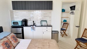 A compact room with a bed, a kitchenette, and a door leading to another room. - Renovated Beach Front Studio - Hawaiian Inn Resort (Daytona Beach Shores)