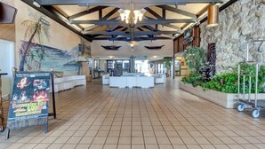 A spacious lobby with a high ceiling, a central reception desk, and a large mural depicting a tropical scene. - Renovated Beach Front Studio - Hawaiian Inn Resort (Daytona Beach Shores)