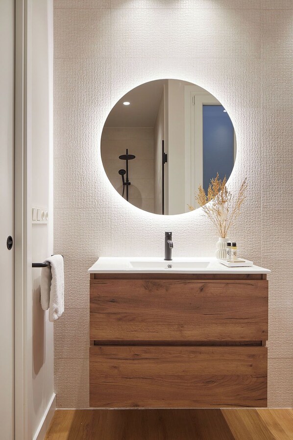 Une salle de bain avec un miroir rond, un lavabo blanc, un meuble-lavabo en bois et un porte-serviettes.