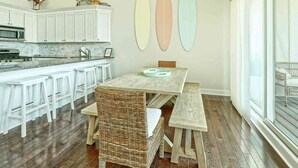 A kitchen with white cabinets, a microwave, and a dining area with a wooden table and wicker chairs. - Bright and Airy Condo.  One block to the Beach.  Great location. (Sea Isle City)