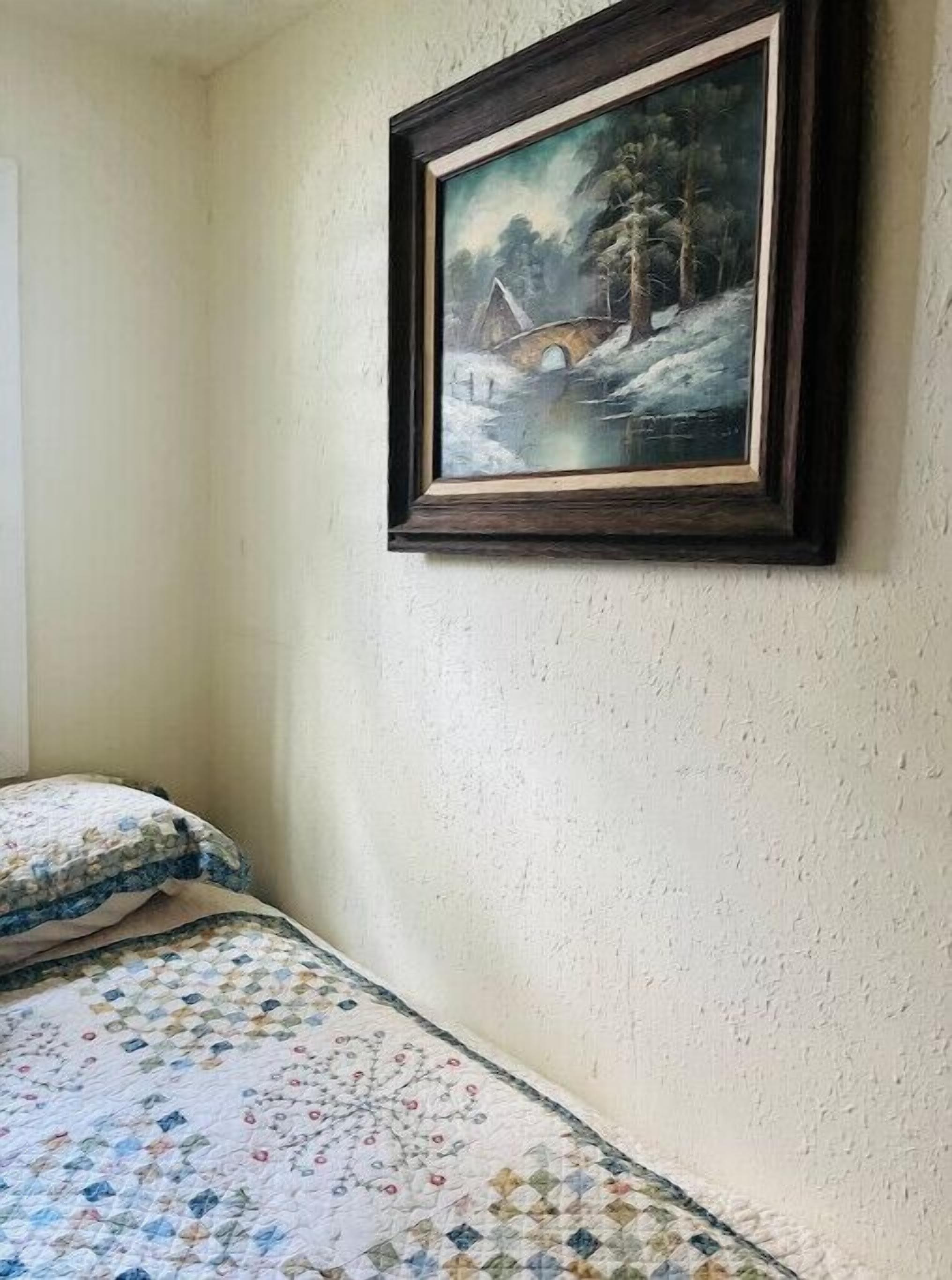 Quarto com cama, colcha e um quadro emoldurado de uma paisagem nevada.