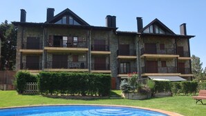 A two-story building with balconies, a swimming pool, and a well-maintained garden.