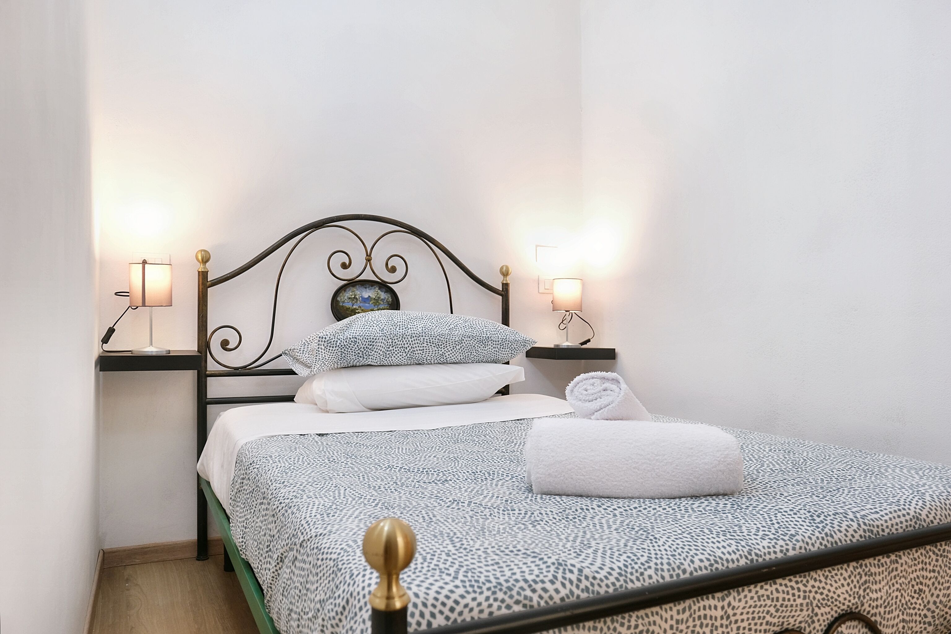 A neatly made bed with patterned bedding, two bedside lamps, and a small decorative item on the headboard.