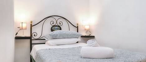A neatly made bed with patterned bedding, two bedside lamps, and a small decorative item on the headboard.