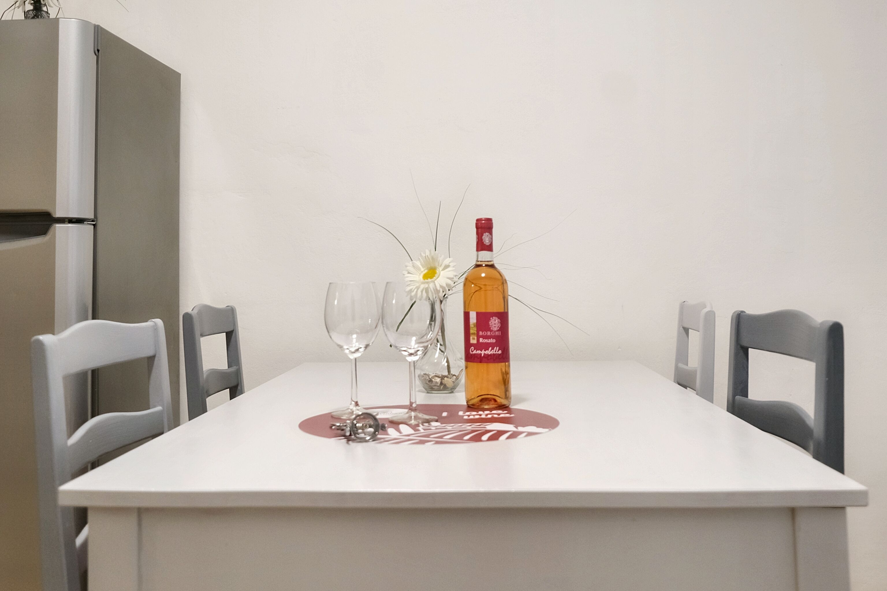 Een eettafel met twee wijnglazen, een wijnfles en een kleine witte bloem.