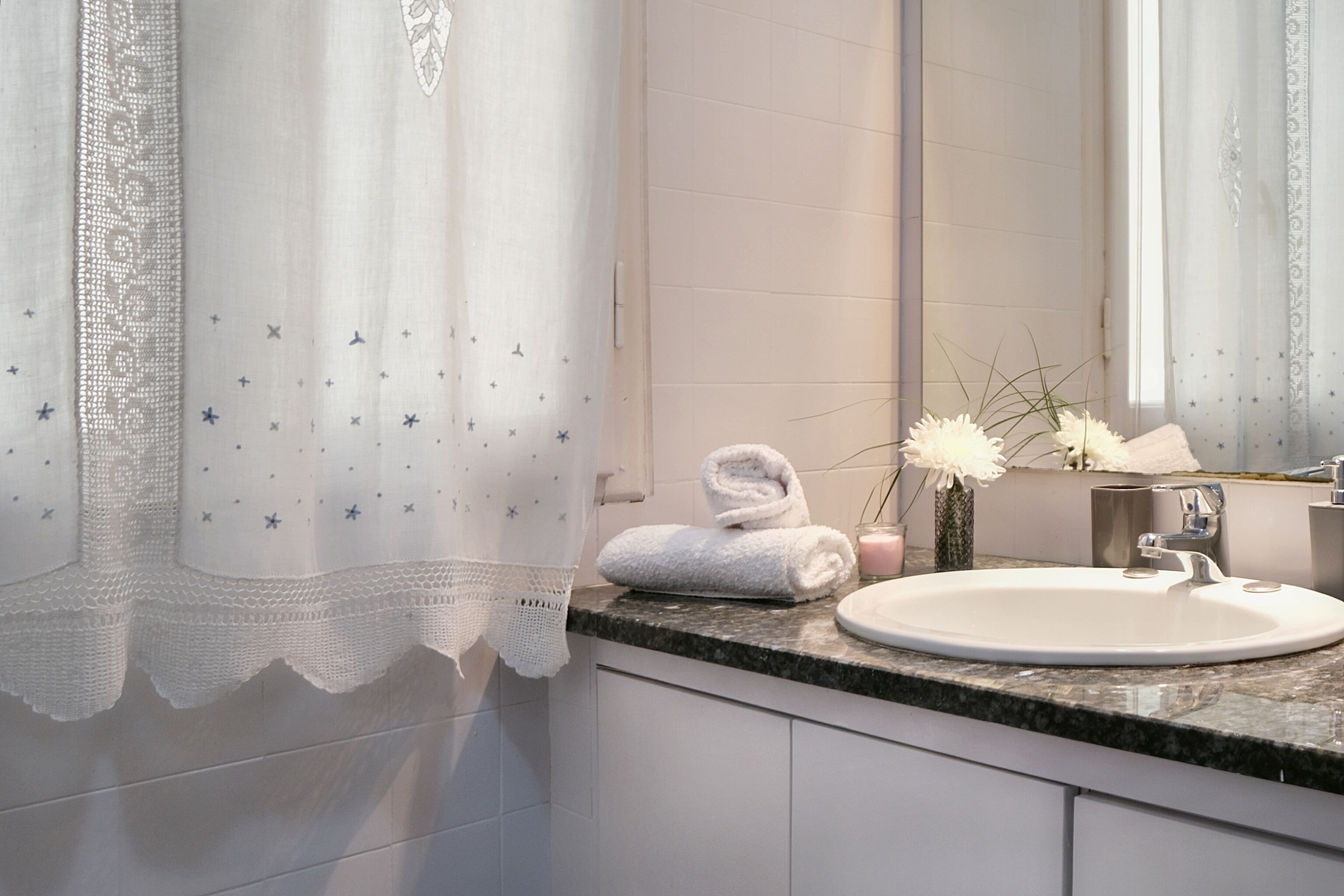 A bathroom with a white sink, a mirror, a towel, and a vase with flowers.