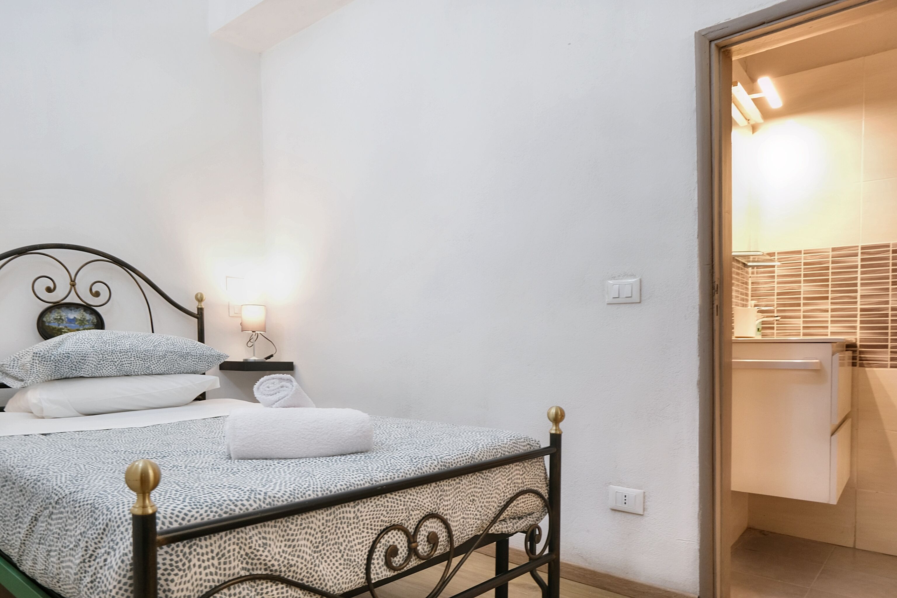 Un letto rifatto con cura, una coperta a motivi, una lampada da comodino e un tavolino con un mappamondo e un libro.