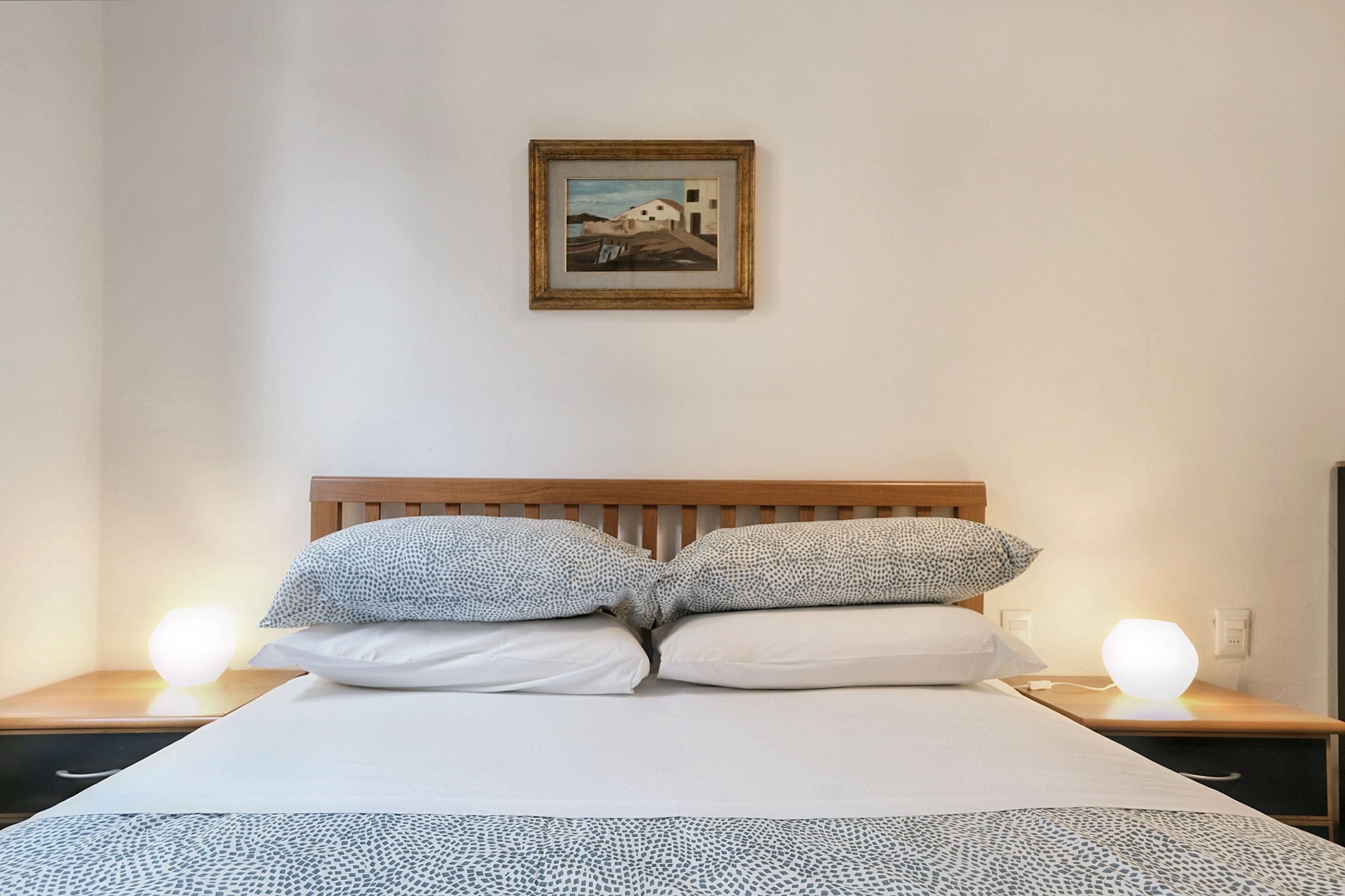 Een net opgemaakt bed met beddengoed met een patroon, een houten hoofdbord en een ingelijst schilderij erboven.
