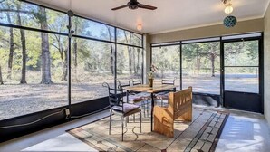 Ein Zimmer mit großen Fenstern, einem Deckenventilator, einem Tisch mit Stühlen und einer Hängelampe.