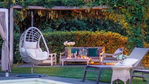 A poolside area with a hanging chair, a sofa, and a table set with candles and flowers.