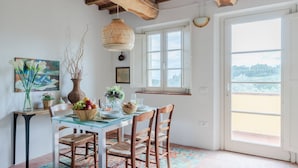 A dining area with a glass table, wooden chairs, and a hanging light fixture.