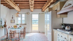 A kitchen with wooden beams, a dining area with chairs and a table, and a view through the open door.