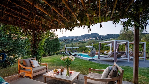 An outdoor seating area with wooden furniture, a pool, and a view of the countryside.