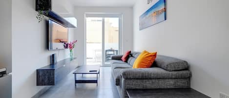 A modern living room with a grey sofa, a coffee table, and a TV mounted on the wall.