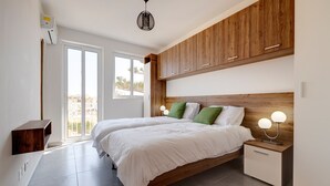 Un dormitorio con dos camas, cabeceros de madera, mesitas de noche con lámparas y vistas a través de la puerta.