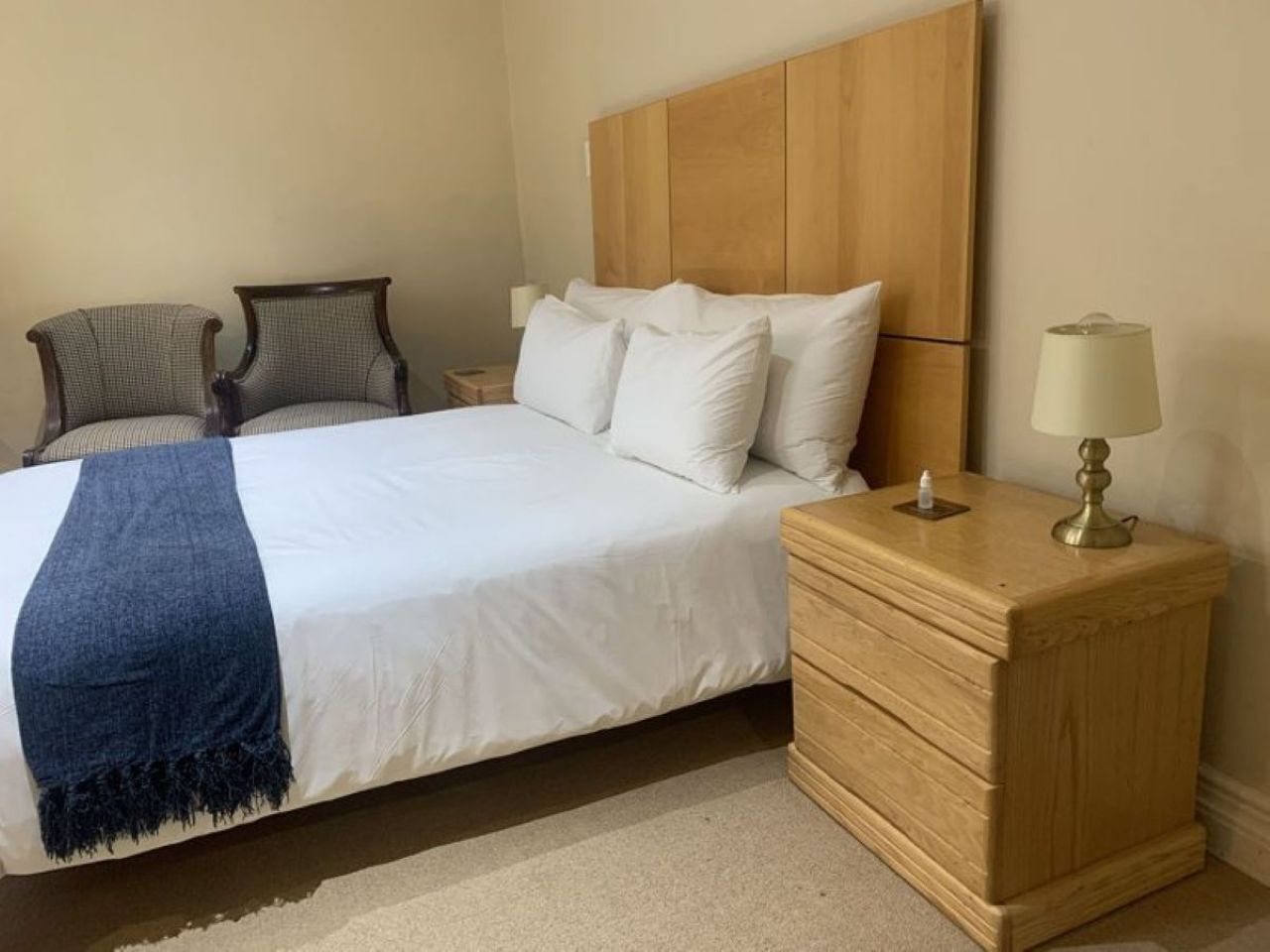 A bedroom with a bed, a wooden nightstand, a lamp, and two chairs.