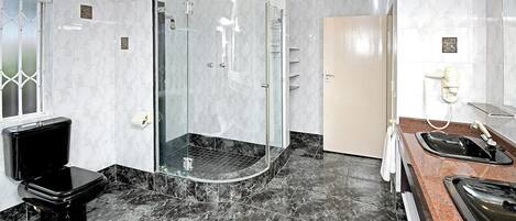 Un baño moderno con ducha acristalada, inodoro negro y lavamanos con espejo.