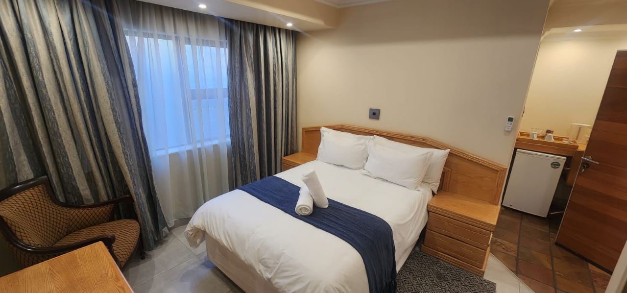 A hotel room with a bed, a chair, a desk, a mini-fridge, and curtains.